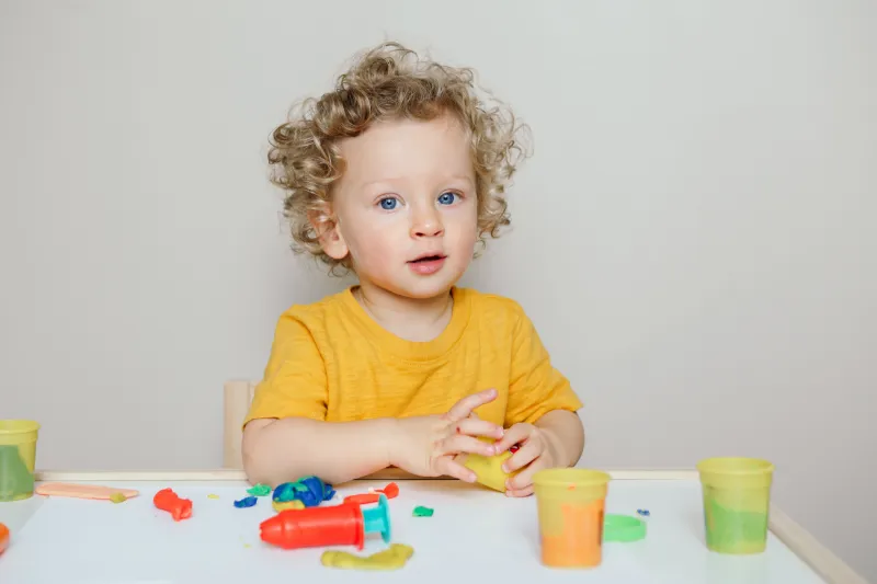 lond curly baby boy child playing with sensor kinetic toy playdough